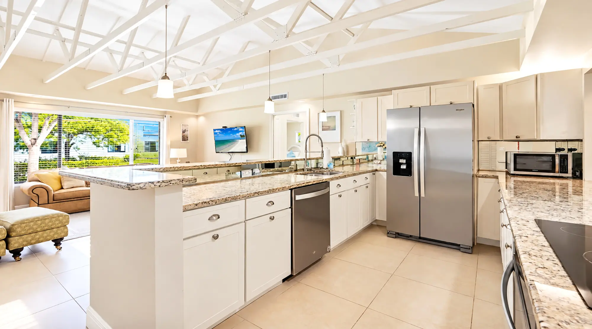 Kitchen with white cabinets, granite countertops, stainless steel appliances, and an open view to a living room with a large window.