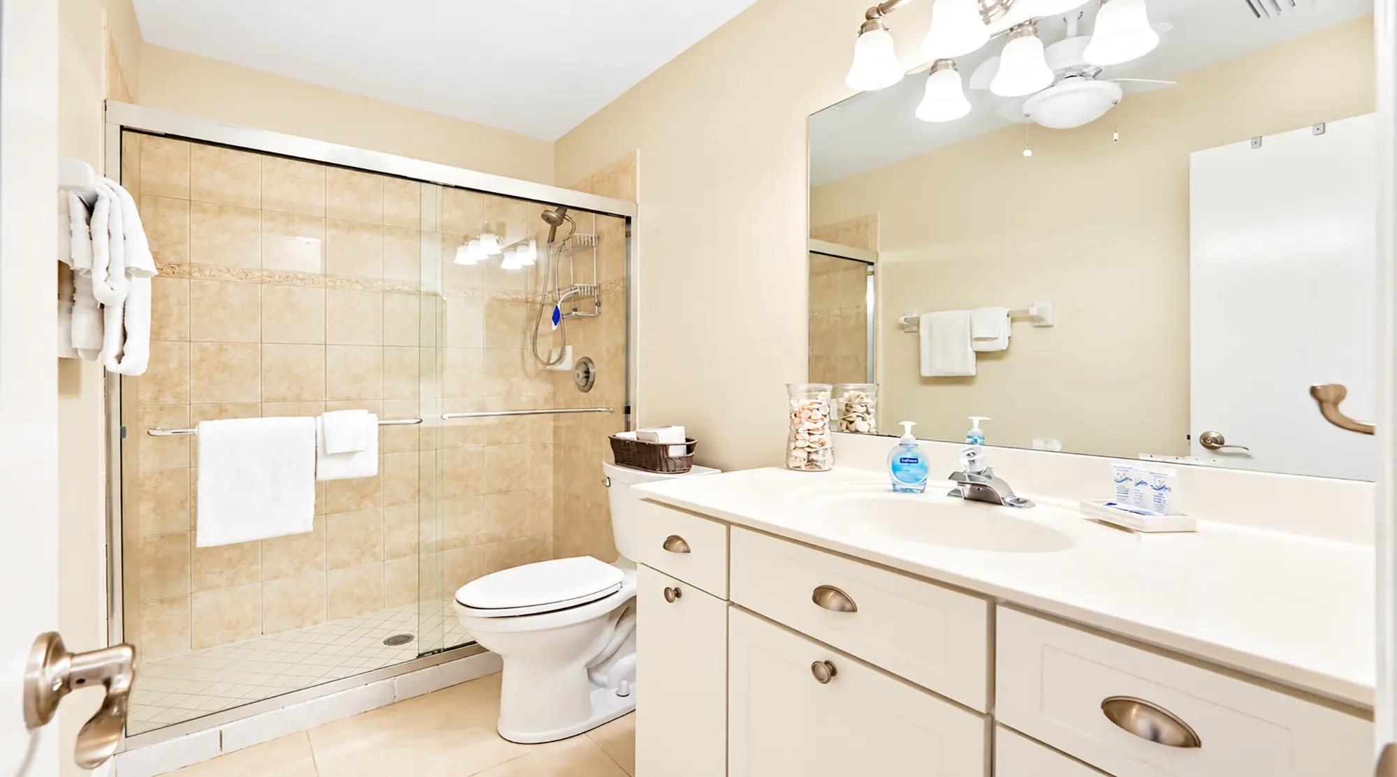 Bathroom with a white vanity sink, toilet, and a glass-enclosed walk-in shower with tan tiled walls.