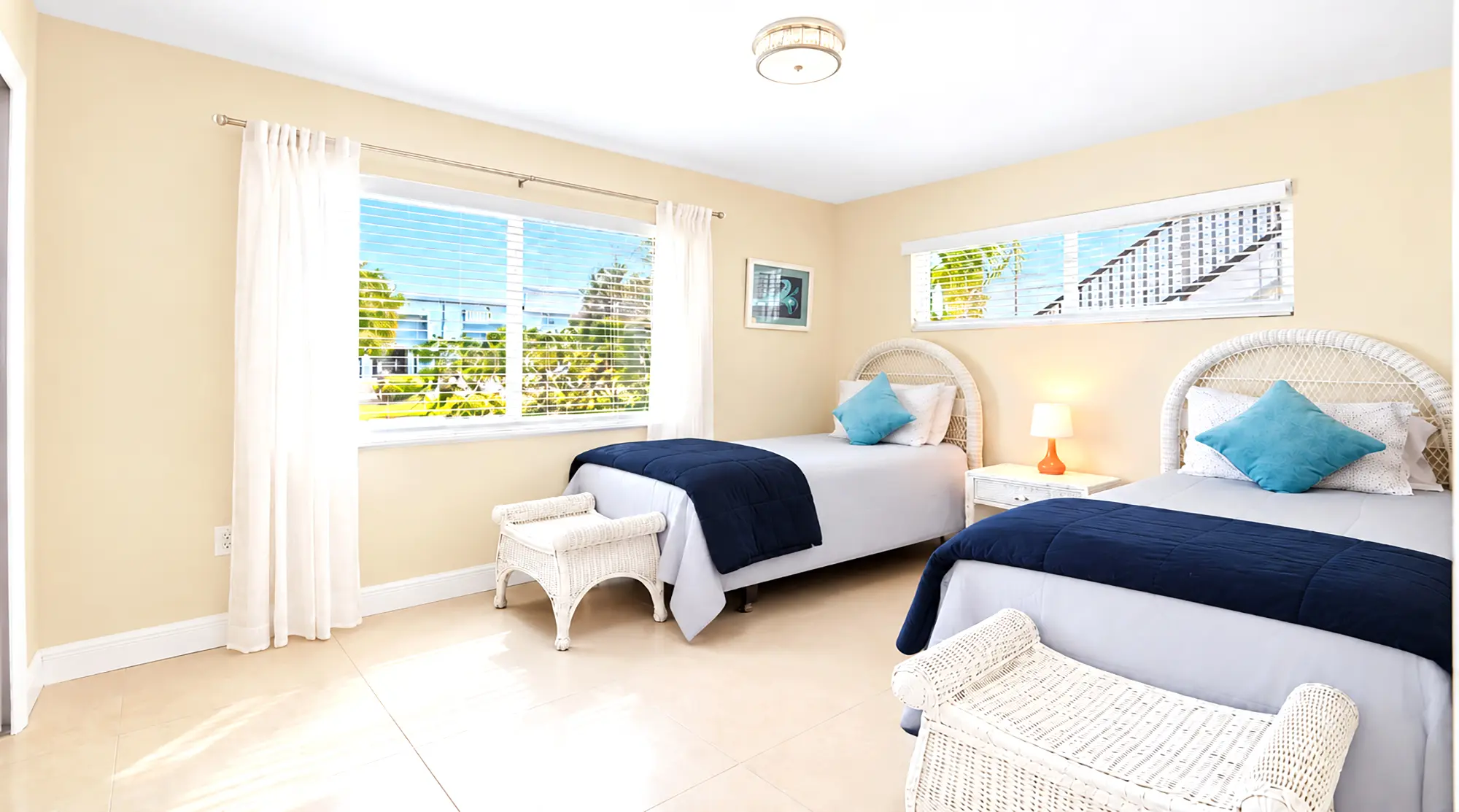 Two twin beds with white wicker headboards, blue bedding, and matching benches in a Naples waterfront vacation rental.