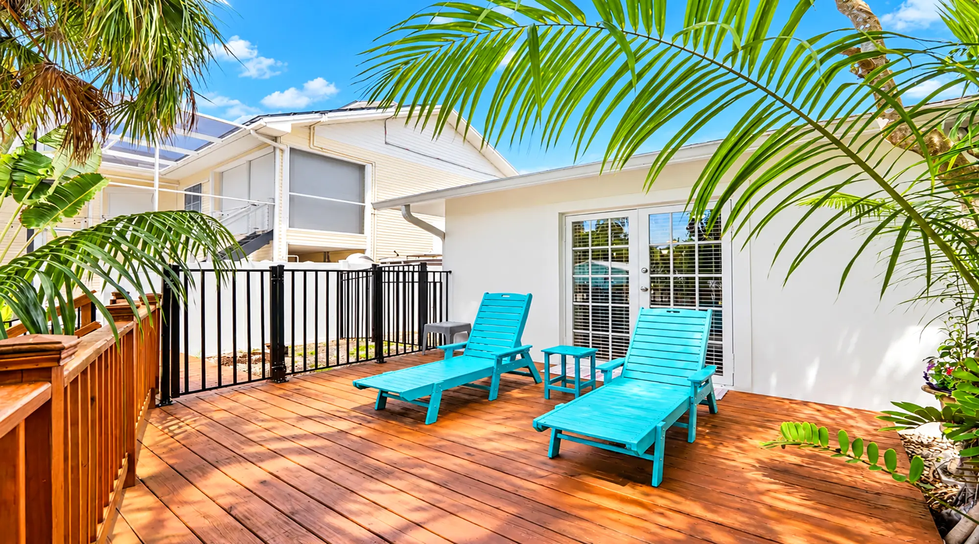 Two bright blue lounge chairs on a wooden deck in front of a white house with glass doors.