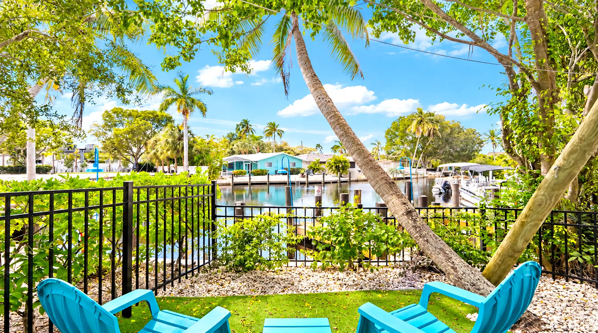 Two blue chairs on a patio overlooking a canal with boat slips and tropical landscaping.