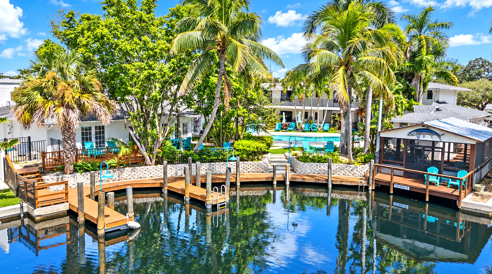 A Naples waterfront vacation rental featuring a swimming pool, wooden docks, palm trees, and surrounding white buildings.