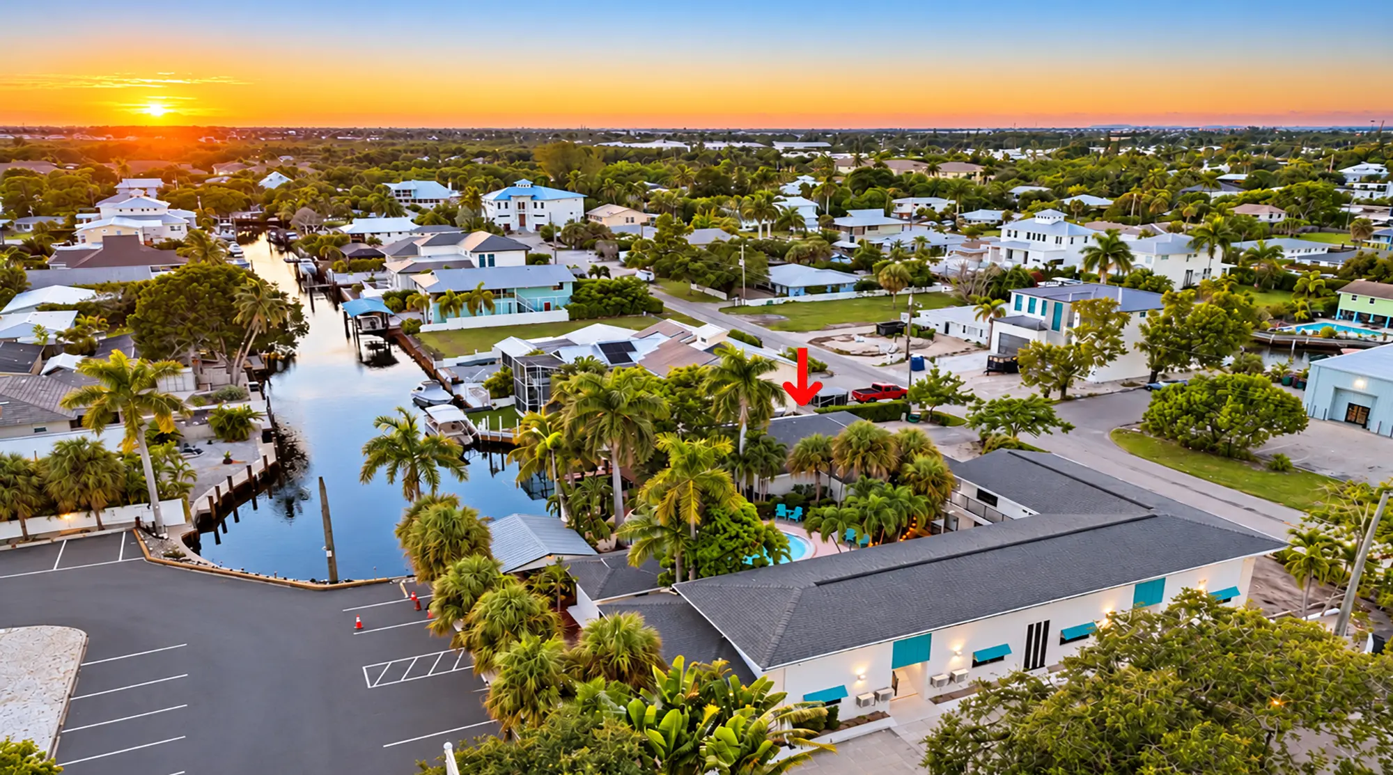 Aerial view of a coastal neighborhood at sunset with a red arrow pointing to a specific house near a canal.